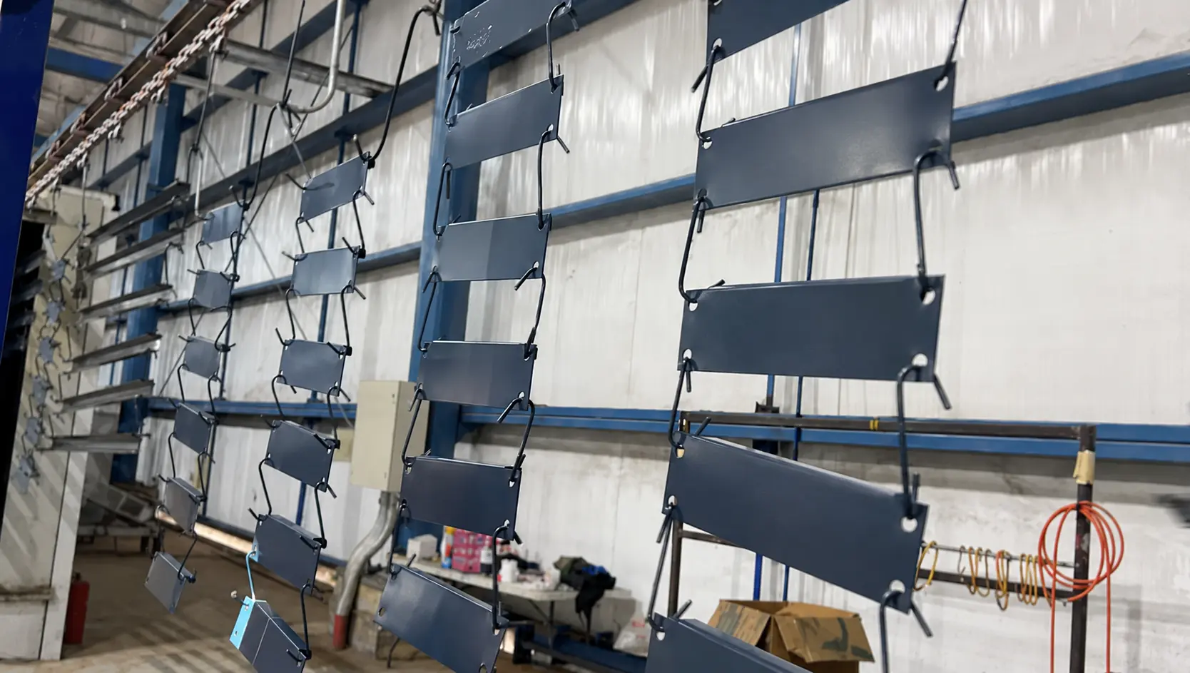 Piezas metálicas con acabado azul grisáceo suspendidas en el transportador